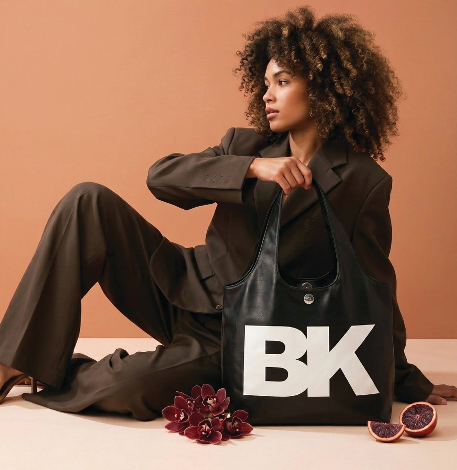 Woman holding a black bag with 'BK' logo on a peach background